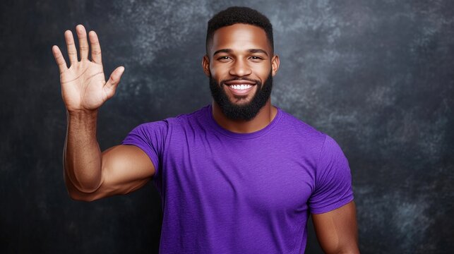man with a beard and a joyful smile waves with his right hand. He is dressed in a purple short-sleeve shirt and is posed against a dark textured backdrop, creating a warm atmosphere