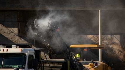Hot steaming asphalt pouring off of the converyor belt of an asphalt milling machine