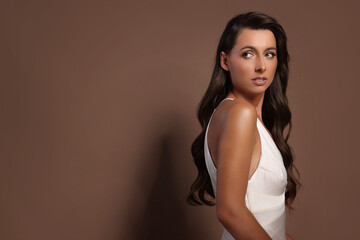 Fototapeta premium Hair styling. Beautiful woman with wavy long hair on brown background, space for text