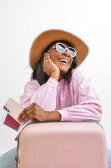 Tourist holding passport and smartphone leaning on suitcase smiling and looking away