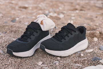 Naklejka premium Black sneakers with a white sock resting on sandy beach during golden hour