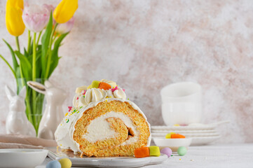 Easter carrot roll cake with cream cheese frosting, decorated chocolate eggs, jellied carrots and sugar sprinkles on top. Traditional carrot roll cake on a concrete background. Easter festive dessert.