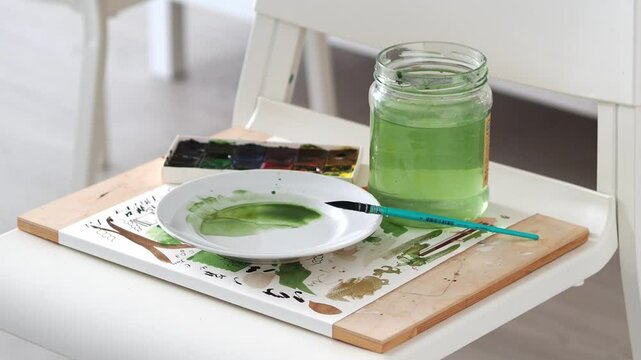 The artist's creative art studio with a place where there is a jar of water, a set of watercolor paints, a palette and brushes.
