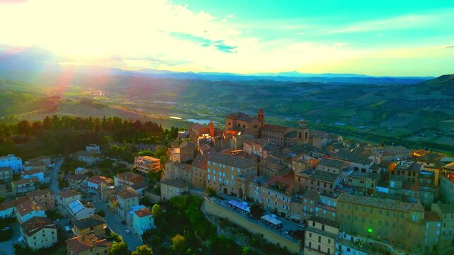 Enchanting aerial pullback shot from Montefiore dell'Aso (AP), bounteous late afternoon sunlight permeates the skies above the Marche hillscapes, illuminating the lands, trees, buildings, roads, cars