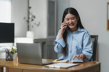 Asian businesswoman talking on phone and using calculator in home office