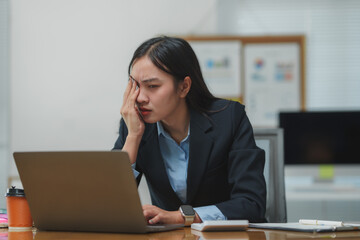 Tired asian businesswoman rubbing eyes while working on laptop in office