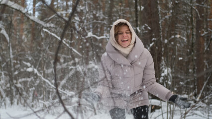 Naklejka premium Young pretty woman in warm winter clothes walking in snowy park