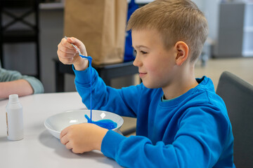 A boy in a blue sweater making blue slime at the table