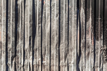 Burnt and deformed corrugated metal sheets with cracks and darkened texture, creating an industrial...
