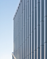 A modern building facade with vertical metal panels creating a geometric pattern under soft daylight. Minimalist and elegant architecture.