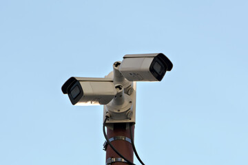 Two surveillance cameras mounted on a pole against a clear blue sky, representing security, monitoring, and urban surveillance systems.