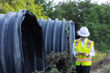 A female engineer wearing a safety vest and hard hat inspects and takes notes on abandoned, damaged...