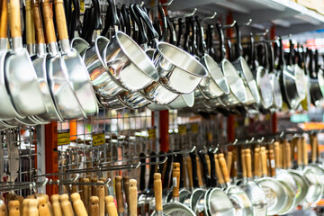 A row of shiny stainless steel ladles with wooden and plastic handles hanging in a kitchenware...