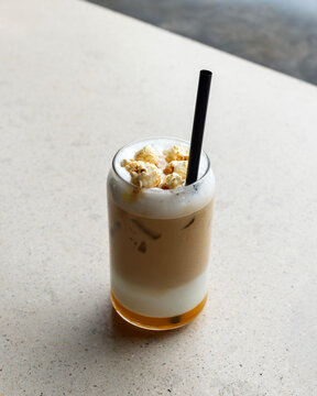Naklejki A unique iced latte topped with caramel popcorn and a black straw, served in a glass, highlighting a creative coffee experience.