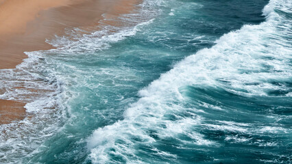 Mighty turquoise waves surge onto the shore, churning up dramatic white foam. The relentless motion of the water highlights the vast power and beauty of the ocean.