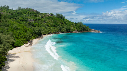 Turquoise ocean with gentle waves hitting a white sandy beach, surrounded by lush greenery and tropical vegetation. Anse Intendance. Seychelles, Mahe.