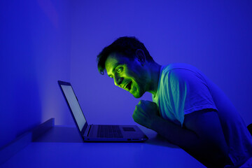 Enthusiastic Man Reacts With Excitement While Using Laptop in Dimly Lit Room