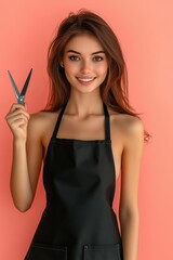 Portrait of a smiling young woman in a black apron holding scissors against a peach-colored background


