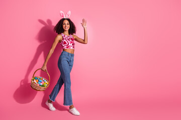 Stylish young woman with bunny ears holding a colorful Easter basket celebrating springtime fun against a pink background.