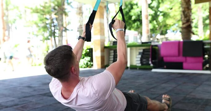 A man at an outdoor gym is performing TRX rows, demonstrating his strength and commitment to fitness