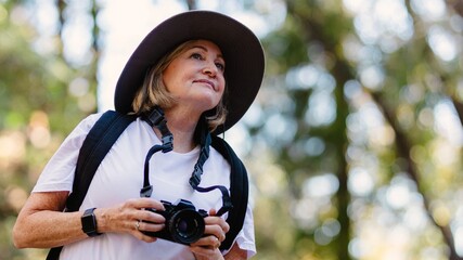 Elderly woman with camera in outdoor nature. Smiling elderly woman with camera in hand exploring nature. Caucasian senior woman adventure in nature with camera. Elderly woman take photo in nature