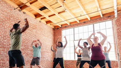 Group exercise class in a brick studio. Diverse participants follow an instructor. Energetic workout session with people raising arms enthusiastically. Diverse people exercising in fitness class.