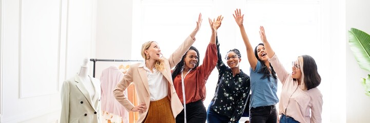 Fototapeta premium Group of diverse women celebrating success. Women high-fiving, smiling, and celebrating. Diverse women in fashion business success, celebrating and smiling together for business success, women power