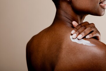 Daily skincare routine. Close-up of a black woman applying lotion on her shoulder. Black woman...