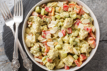Healthy pesto salad with boiled chicken breast, fresh vegetables and almonds close-up in a plate on the table. Horizontal top view from above