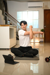Happy asian man stretching his arms while following an online workout on digital tablet