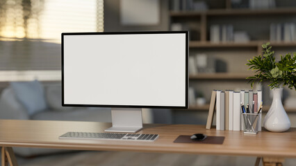 The white screen computer on the wooden table with books and decors in the bedroom or living room.