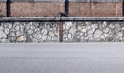 Grunge surrounding wall at the roadside. It is made of large white rocks in the lower side  and bricks in the upper. Street in front. Background for copy space