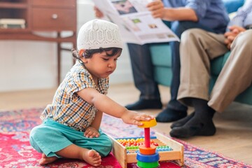 Young muslim child playing with colorful toys on a rug. Child focused on stacking rings. Playful...