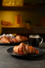 Fresh baked croissants and black coffee on a kitchen table.