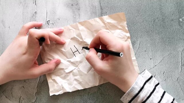Top view of a young woman's hands, writing the word help on a crumpled piece of paper with an appeal to call 911 for rescue