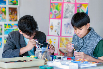 Learning to use poster color to draw various pictures of asian boys on a table outside classroom...