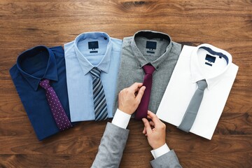 Four neatly folded dress shirts with ties on a wooden surface. Shirts and ties in various colors....