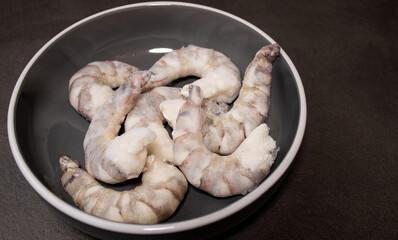 Frozen raw tiger prawns shrimps in a grey bowl on grey kitchen table 
