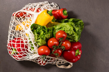 Close up of fresh seasonal vegetables in an eco net shopper bag on grey kitchen table