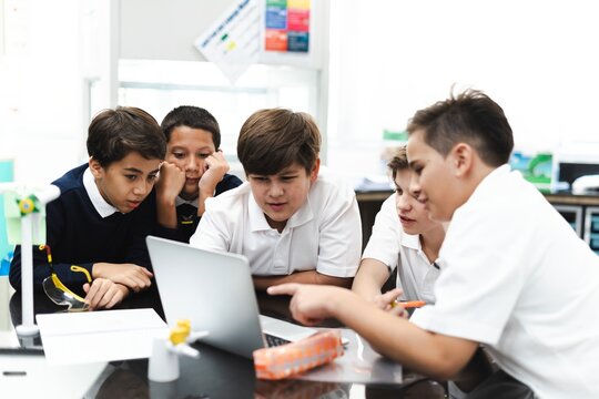 Group of student boys focus on laptop, collaborate in classroom. Boys in school uniforms teamwork, learn together, discuss ideas in classroom. Student focus on group project, work together on laptop