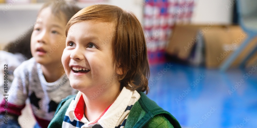 Poster Closeup happy Caucasian boy smiling and sitting with other children in classroom. Boy in classroom with other children. Student boy enjoy lesson in classroom. Student boy smiling in classroom.