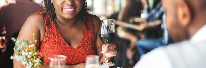 A black woman enjoying a glass of wine at a restaurant. She is smiling and holding a wine glass. The setting is a cozy restaurant with a warm atmosphere. Black couple celebrating at restaurant.