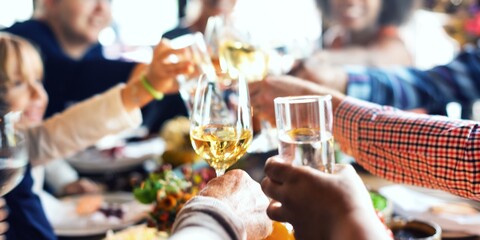 A group of people clinking glasses in a celebratory toast. Diverse hands holding wine glasses. Festive atmosphere with friends enjoying a meal together. People toasting and celebrating at dinner.