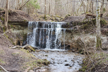 
a small waterfall flowing over a rocky bank in the middle of a forest.