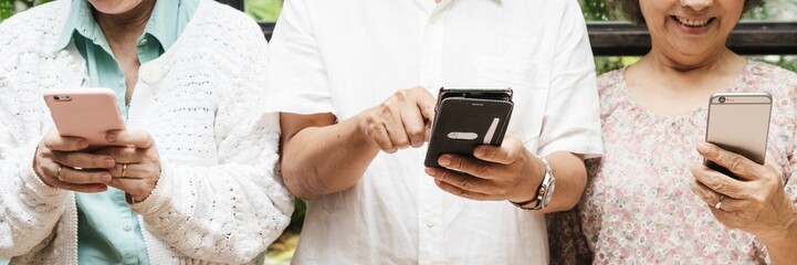 Three elderly individuals using smartphones, focusing on their hands. They are engaged with their phones, showcasing technology use among seniors. Senior people texting on mobile phones.