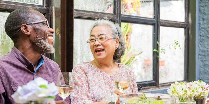 Elderly couple enjoying wine and laughter. Happy elderly pair sharing a meal. Joyful elderly man and woman with wine, enjoying each other's company. Diverse senior people drinking wine at lunch.