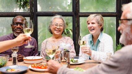 Group of diverse seniors enjoying a meal together, smiling and toasting with wine. Happy elderly friends, diverse gathering, joyful meal, senior celebration. Happy retired people celebrating with wine