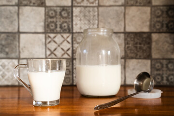 A glass with fresh homemade milk. Large glass jar filled with milk sits on a wooden surface on the background. Rustic, traditional, natural living, farm-fresh products, dairy products, milk day.