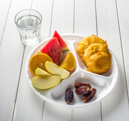 Typical asian meal or snack contains Pakora, fruits, snacks and dates are consumed for Iftar ritual . A food served in a disposable plate to distribute to break fast of Ramadan. © Telsa
