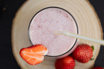 Top view of strawberry smoothie in a glass cup next to scattered strawberries on a rustic dark...